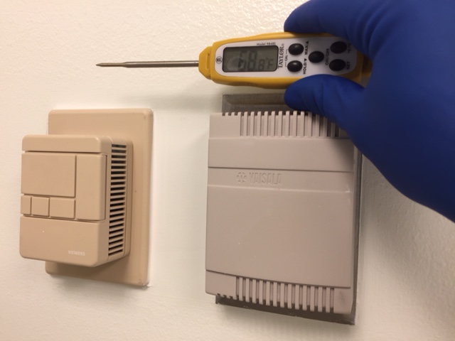 Picture of a person checking wall thermostats with a temperature gauge